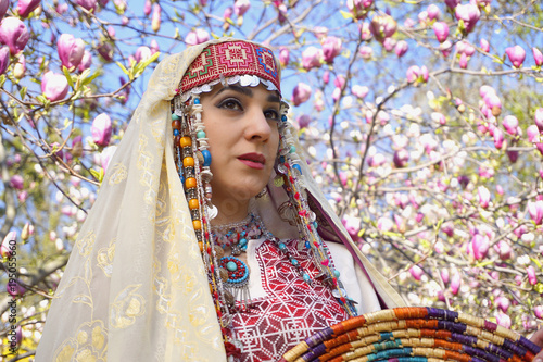 Girl against of magnolia flowers in national Palestinian costume, with head covered. 