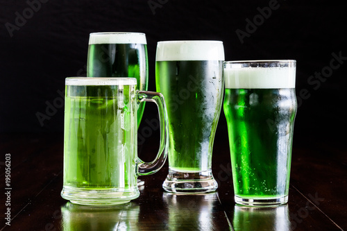 4 beer glasses, stein beer mug, Belgian ale, classic pilsner and English pub with green beer on rustic wood table.