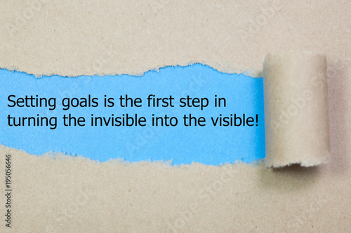 Motivational quote Setting goals is the first step in turning the invisible into the visible , appearing behind torn paper.