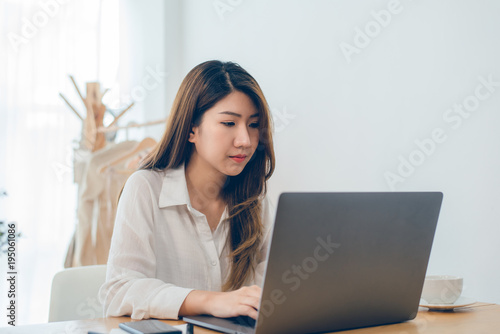 Beautiful young smiling Asian woman working on laptop while at home in office work space. Businesswoman working from home via portable computer writing on keyboard. Enjoying time at home.