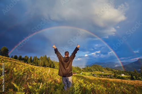 young guy  a tourist  raised his hands and thumbs up  rejoicing at the seen rainbow
