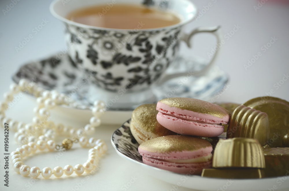 Gold and pink French macarons with pearls and a fine bone china cup with black flowers. Luxurious treats.
Gold and pink French macarons with pearls and a fine bone china cup with black flowers. Luxurious treats.