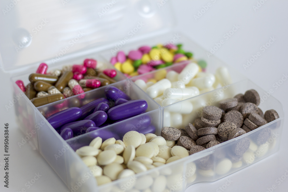multicolored tablets and capsules in transparent container on light background multicolored tablets and capsules in transparent container on light background