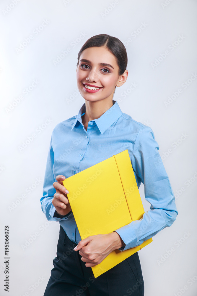 Businesswoman standing with yellow folder on gray background Businesswoman standing with yellow folder on gray background