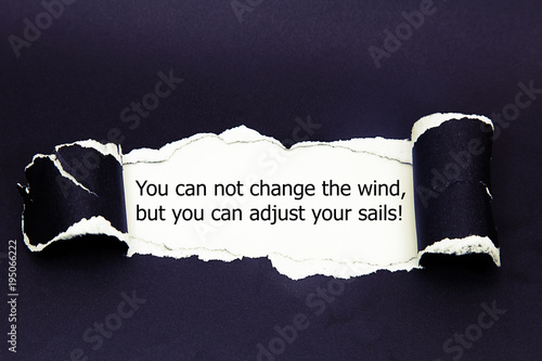 Motivational quote You can not change the wind but you can adjust your sails, appearing behind torn paper.