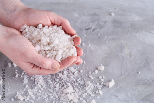 Sea salt crystals in women hand on white background, overhead, close-up