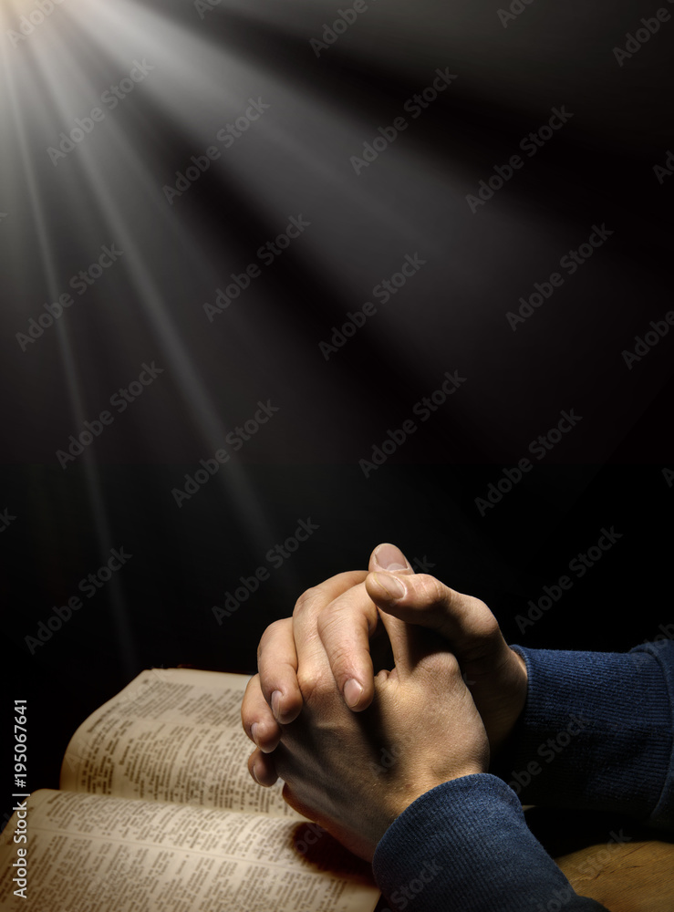 Fototapeta premium Hands folded in prayer over Scriptures