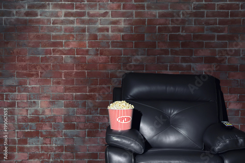 Cinema armchair with popcorn and remote control for home theatre on brick wall background. Watching movie