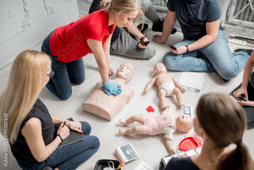 Young woman instructor showing how to make chest compressions with dummy during the first aid group training indoors photo
