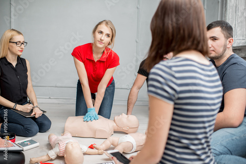 Young woman instructor showing how to make chest compressions during the first aid training indoors