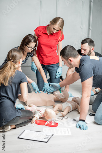 Group of people learning how to make first aid heart compressions with dummies during the training indoors photo