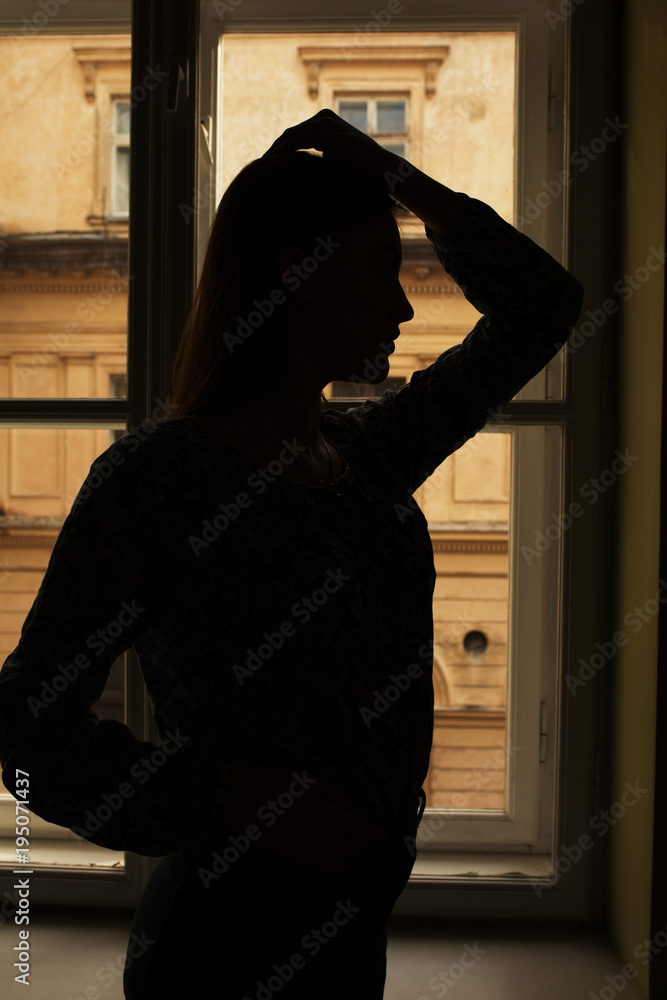 Naklejka premium Silhouette of slim model standing at the window