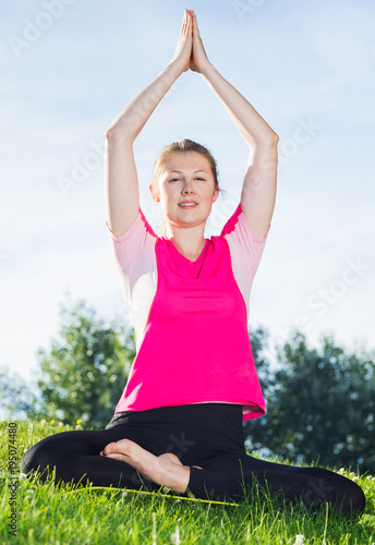 Smiling adult female in pink T-shirt is sitting and meditating © JackF