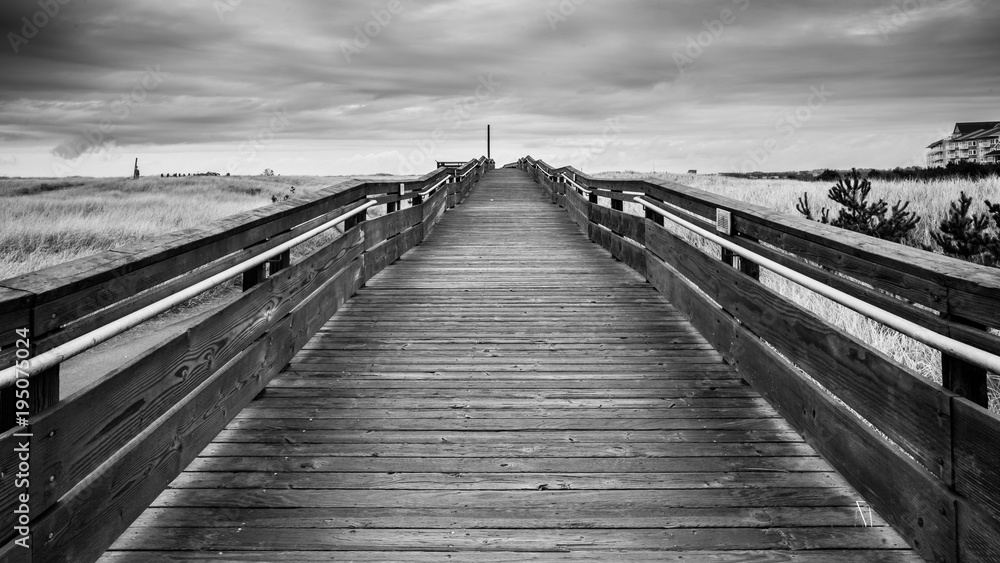 Black And White Of A Wood Bridge That Leads To The Horizon By The Horizon Above Large Green Tall Grass Field Under The Stormy Sky And Rolling Clouds In Long Beach Washington