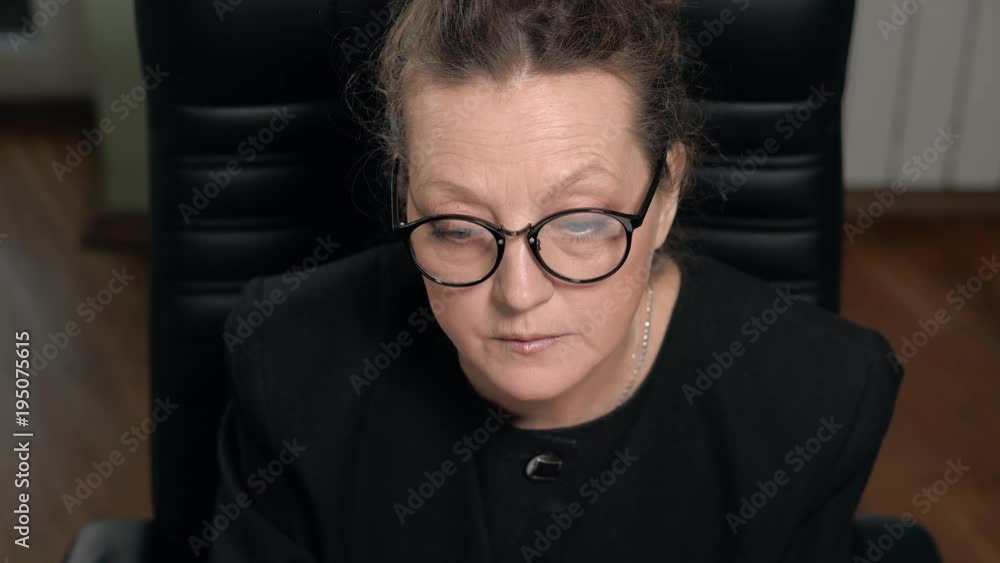 Mature woman brunette in glasses works on computer sitting in chair Mature woman brunette in glasses works on computer sitting in chair