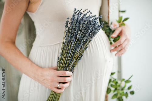 Pregnant woman with bouquet of lavender flowers holds hands on belly outdoors. Pregnancy, parenthood, preparation and expectation concept