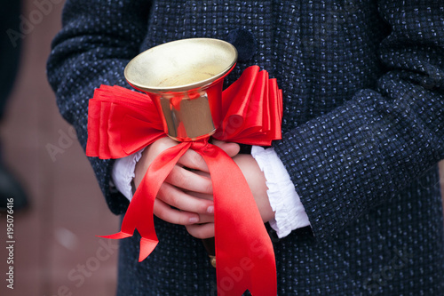Close up shot of pupil hands holding school bell with red ribbon. Back to school concept. First september