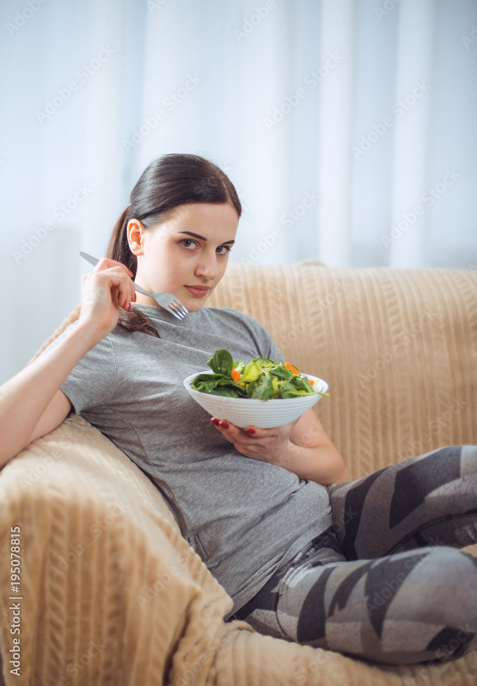 Woman in sportswear with plate of vegetarian vegetable salad. Young sporty model at livingroom. Health, beauty and fitness concept. Woman in sportswear with plate of vegetarian vegetable salad. Young sporty model at livingroom. Health, beauty and fitness concept.