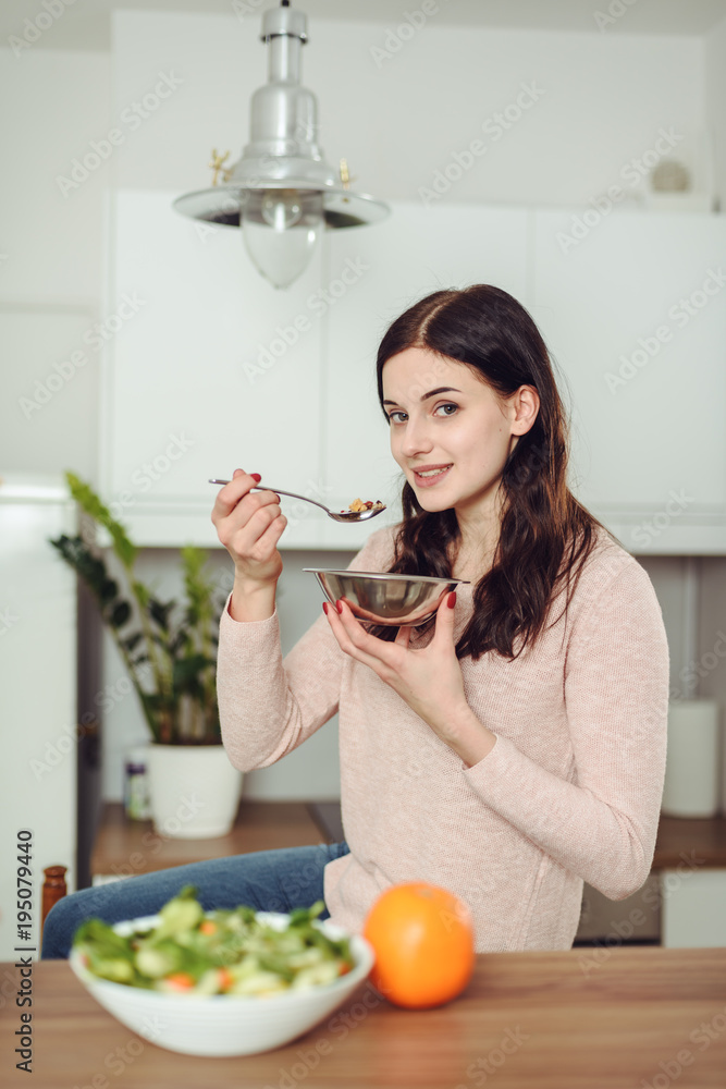 Smiling young woman in the kitchen near desk and eats cereals. Healthy life concept Smiling young woman in the kitchen near desk and eats cereals. Healthy life concept