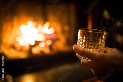 Hand holding whiskey glass at fireplace