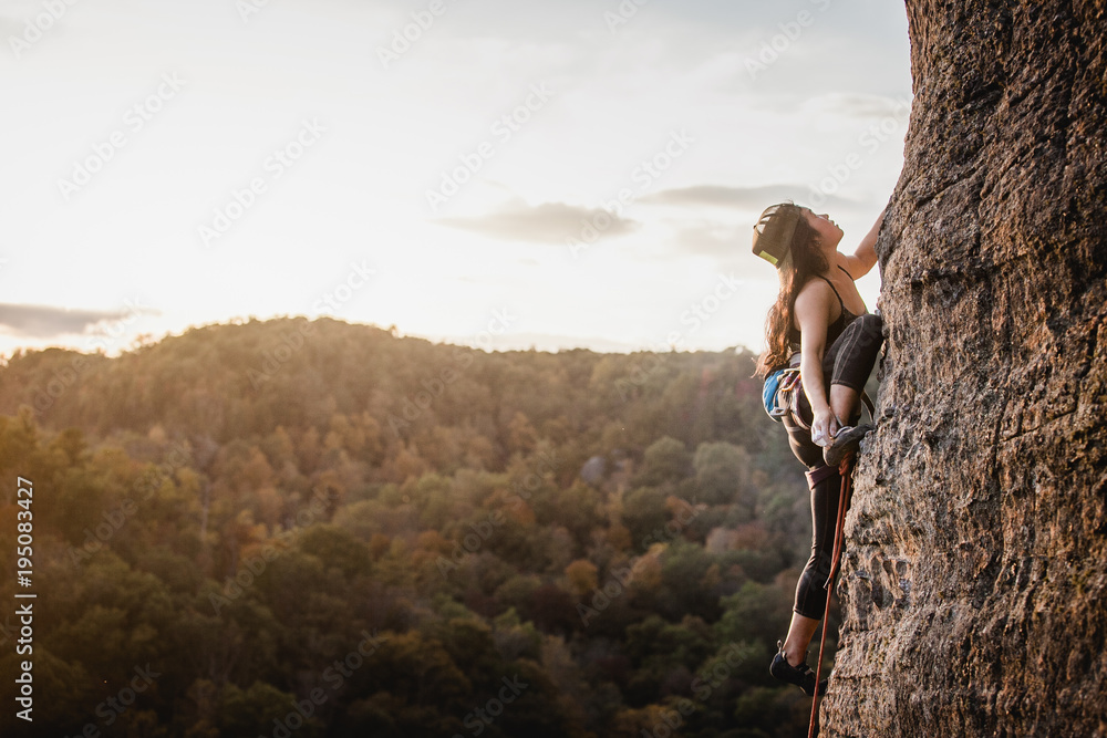 Female climber on a wall climbing at sunset - obrazy, fototapety, plakaty 