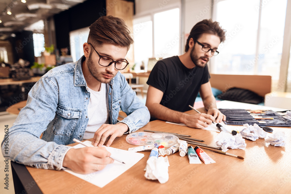 Two freelancer men drawing on paper with pencils at desk.