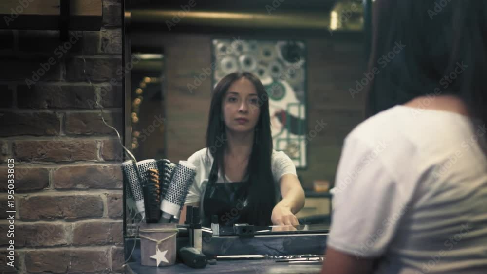 Beautiful brunette is looking in the mirror, gently touches her hair, takes professional metal scissors in hands, turns around on chair and looks away. Slow mo Beautiful brunette is looking in the mirror, gently touches her hair, takes professional metal scissors in hands, turns around on chair and looks away. Slow mo