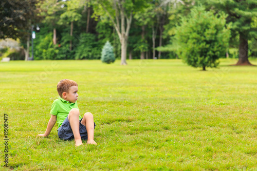 barefoot boy sitting on the lawn. cute kid in the park. Looking away. copy space for your text