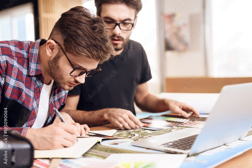 Two freelancer men taking notes at laptop at desk. Two freelancer men taking notes at laptop at desk.