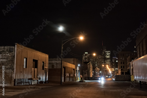 Urban city street with vintage industrial warehouses and the Chicago skyline with the moon at night © Bruno Passigatti