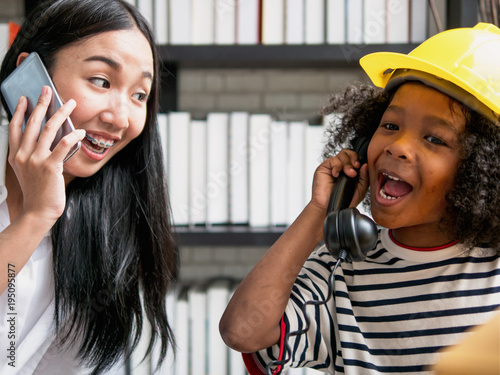 Young Asian nanny playing telephone calling with cute curly hair boy after school photo