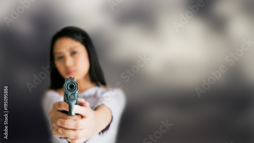 Young Asian female with handgun in hands point gun to target in front