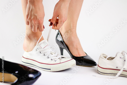 Girl changing shoes. Removes black shoes and wears white sneakers. Tired feet of shoes. Close up. Isolated on a white background