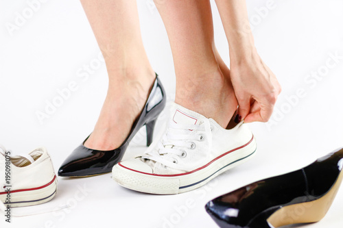 Girl changing shoes. Removes black shoes and wears white sneakers. Tired feet of shoes. Close up. Isolated on a white background