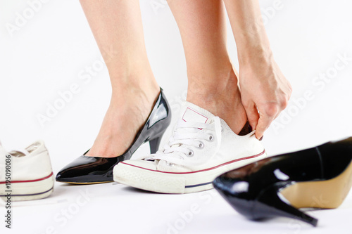 Girl changing shoes. Removes black shoes and wears white sneakers. Tired feet of shoes. Close up. Isolated on a white background