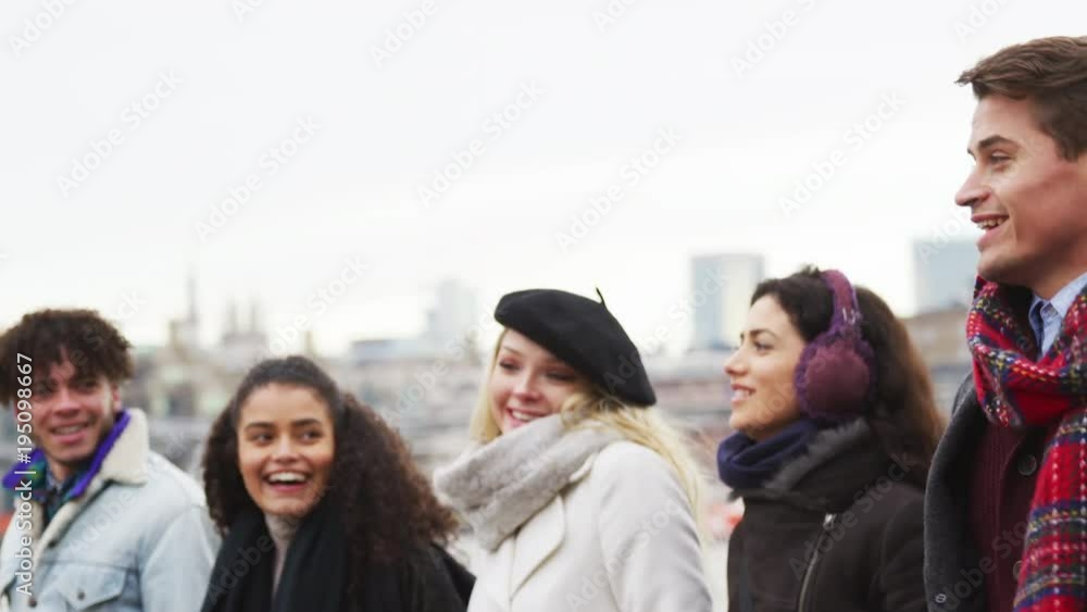 Friends Walking Along South Bank On Winter Visit To London Friends Walking Along South Bank On Winter Visit To London