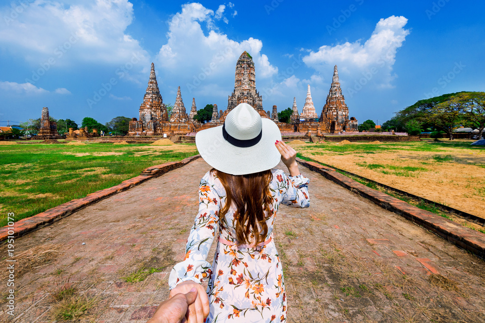 Fototapeta premium Woman holding man's hand and leading him to Ayutthaya Historical Park, Wat Chaiwatthanaram Buddhist temple in Thailand.