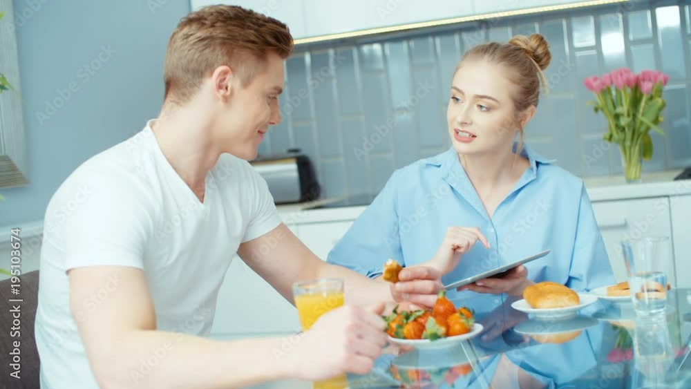 Young couple using digital tablet while having breakfast at kitchen table Young couple using digital tablet while having breakfast at kitchen table