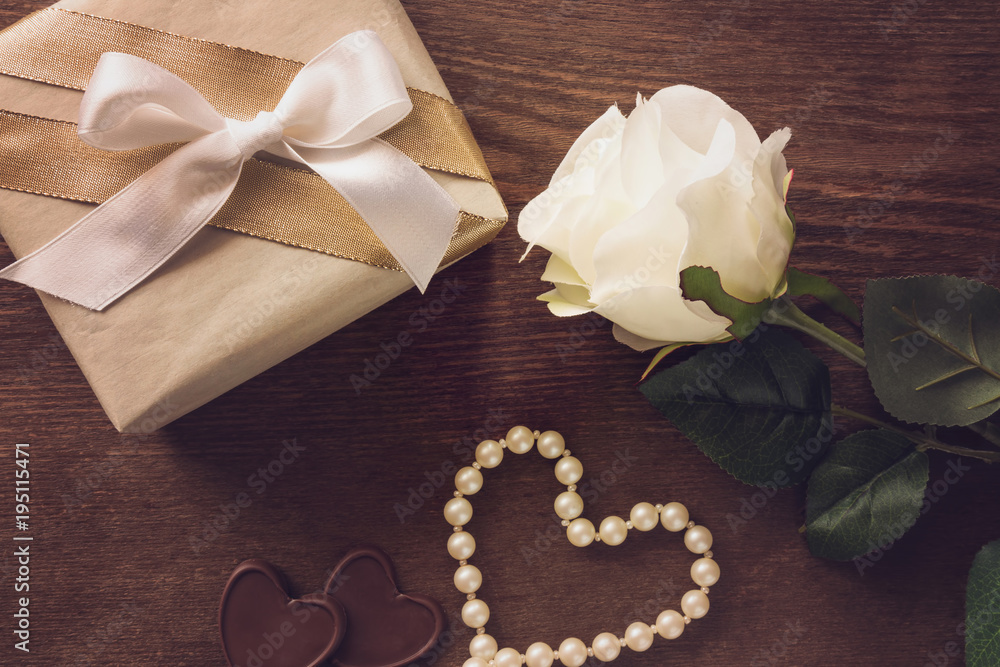 Beautiful rose, gift box with white ribbon and beads on brown wooden table. Lovely, romantic surprise for beloved. Woman's day and relationship concept. Decorative artificial flower.