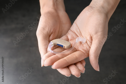 Woman holding hearing aid on grey background, closeup