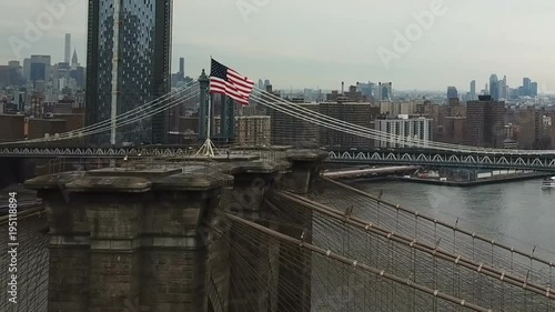 aerial helicopter view over East River with Brooklyn Bridge American flag turning toward Manhattan skyline with Freedom Tower in New York City NYC in 1080 HD