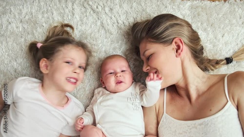 Happy family relaxing on the floor at home. Young cheerful mom with little daughter kissing newborn baby.