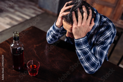 high angle view of drunk man sitting at table with bottle and glass of alcohol at home