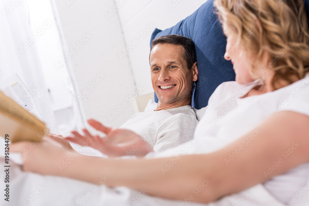 side view of couple reading newspaper and book in bed at home