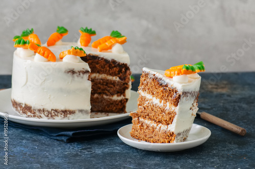 Carrot cake with cream cheese frosting decorated with carrot marmalade serving on a plate on a blue stone background.