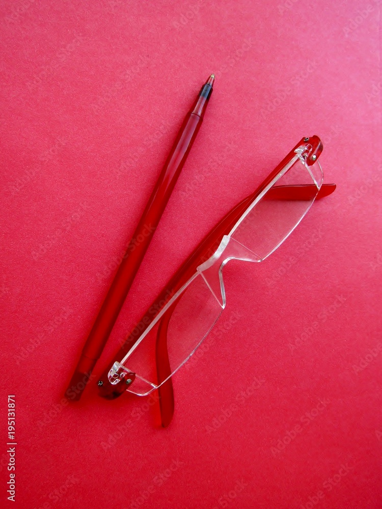 Red reading eyeglasses and red pen on red paper background Red reading eyeglasses and red pen on red paper background