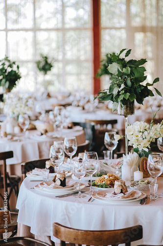 A decorated rustic wedding table with a white tablecloth of porcelain plates with glasses, decorated with flowers with banquet dishes and Viennese chairs