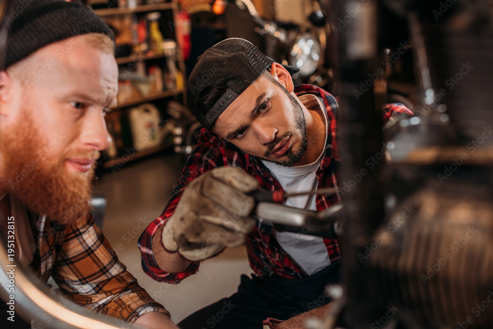 close-up shot of handsome mechanics repairing motorcycle together at garage