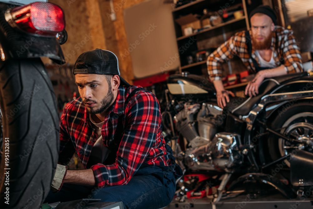 focused mechanic fixing motorcycle while his colleague standing on background