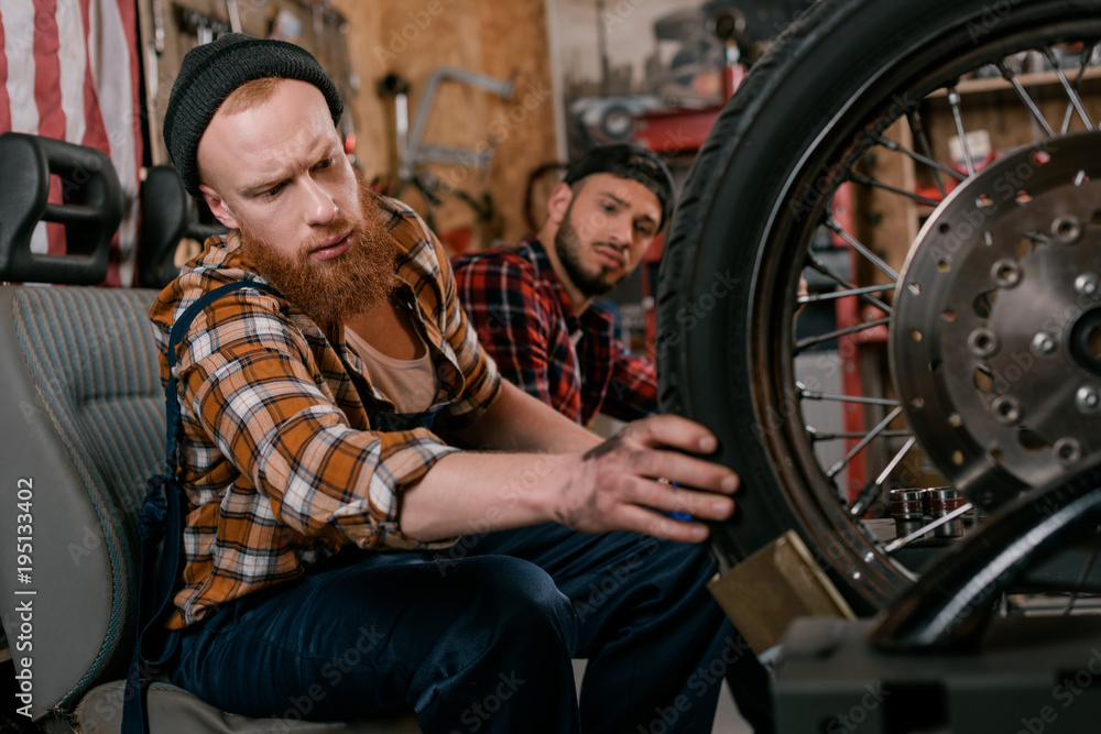 handsome mechanics examining wheel of motorcycle at garage